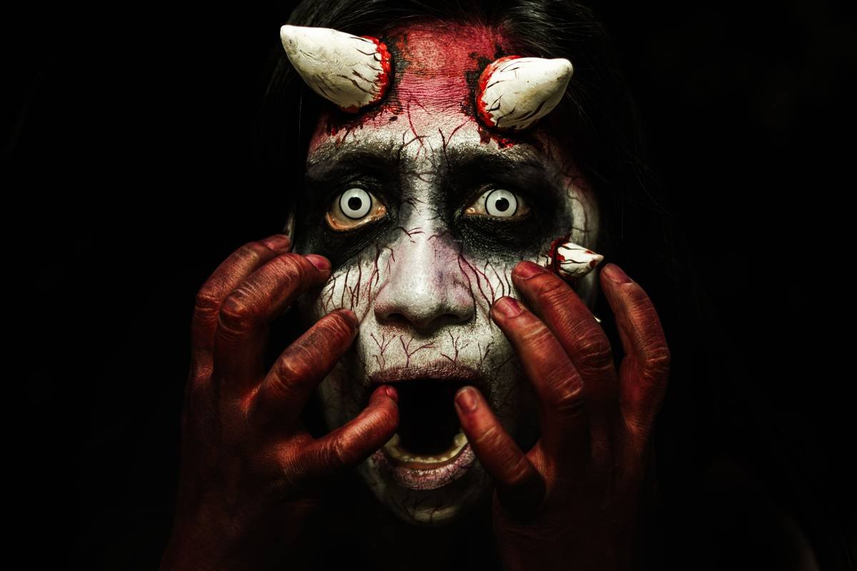 Close-up of an artist applying SFX makeup for monsters with brushes and silicone prosthetics on a model's face