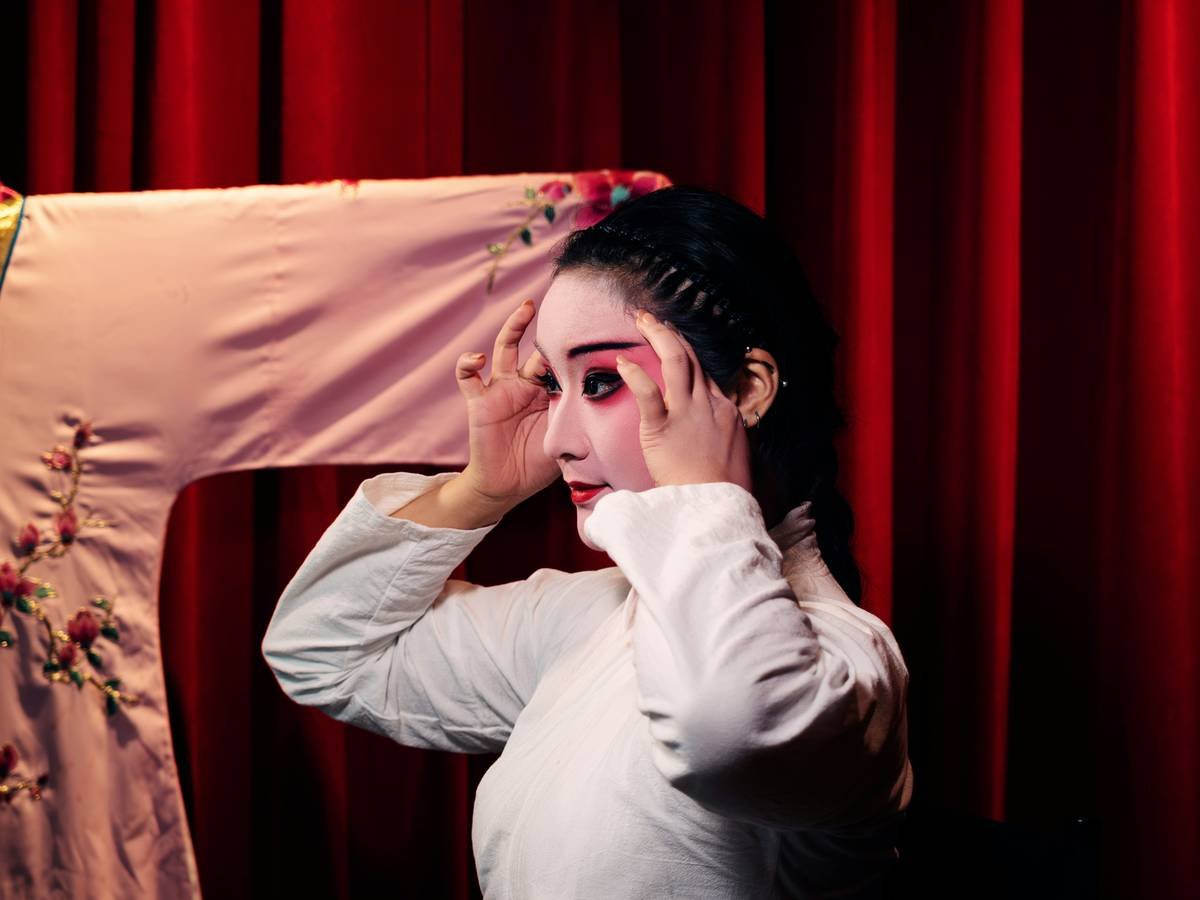 Artist applying festival performance makeup with brushes and vibrant pigments on a model's face outdoors